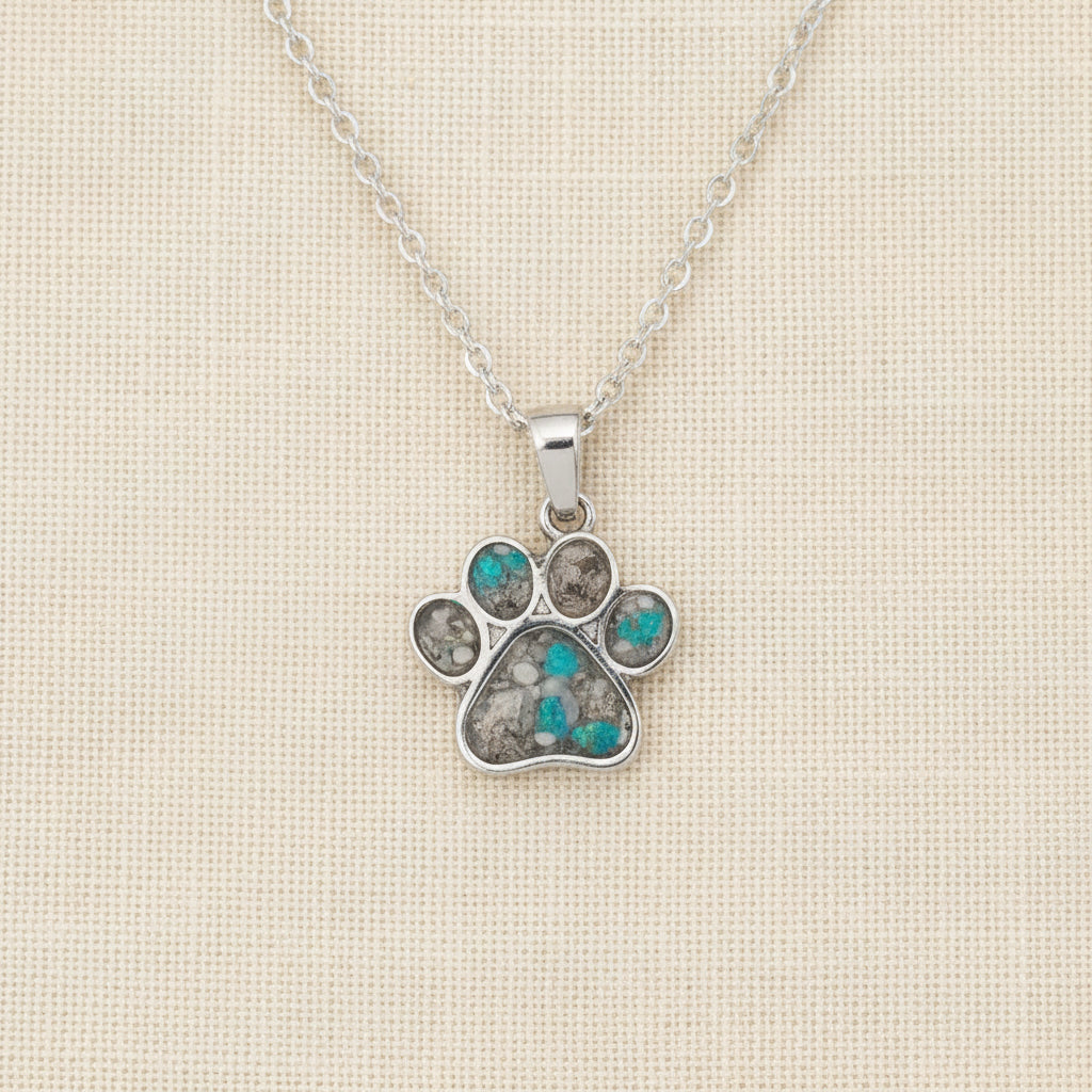 Silver paw print necklace with gemstones on a white surface with pink flowers in the background