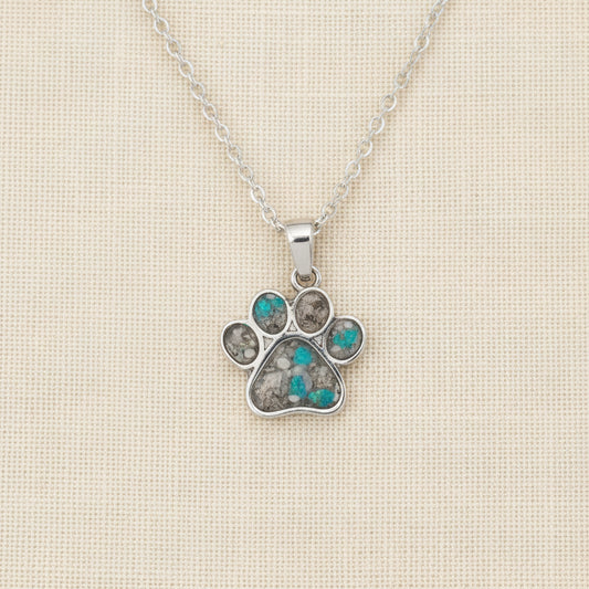 Silver paw print necklace with gemstones on a white surface with pink flowers in the background
