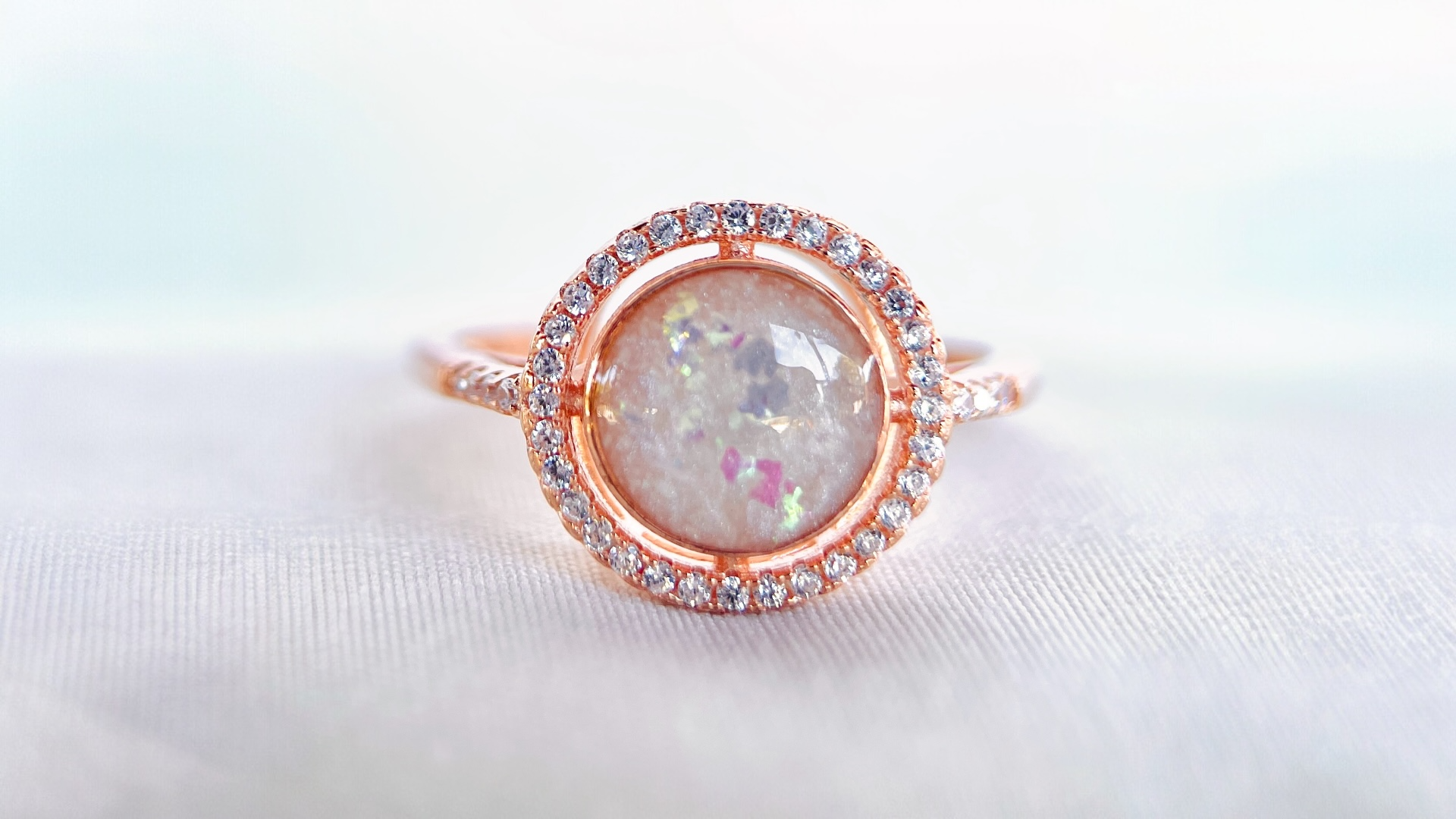 Rose gold ring with a large breast milk gemstone and smaller CZ stones on a white background