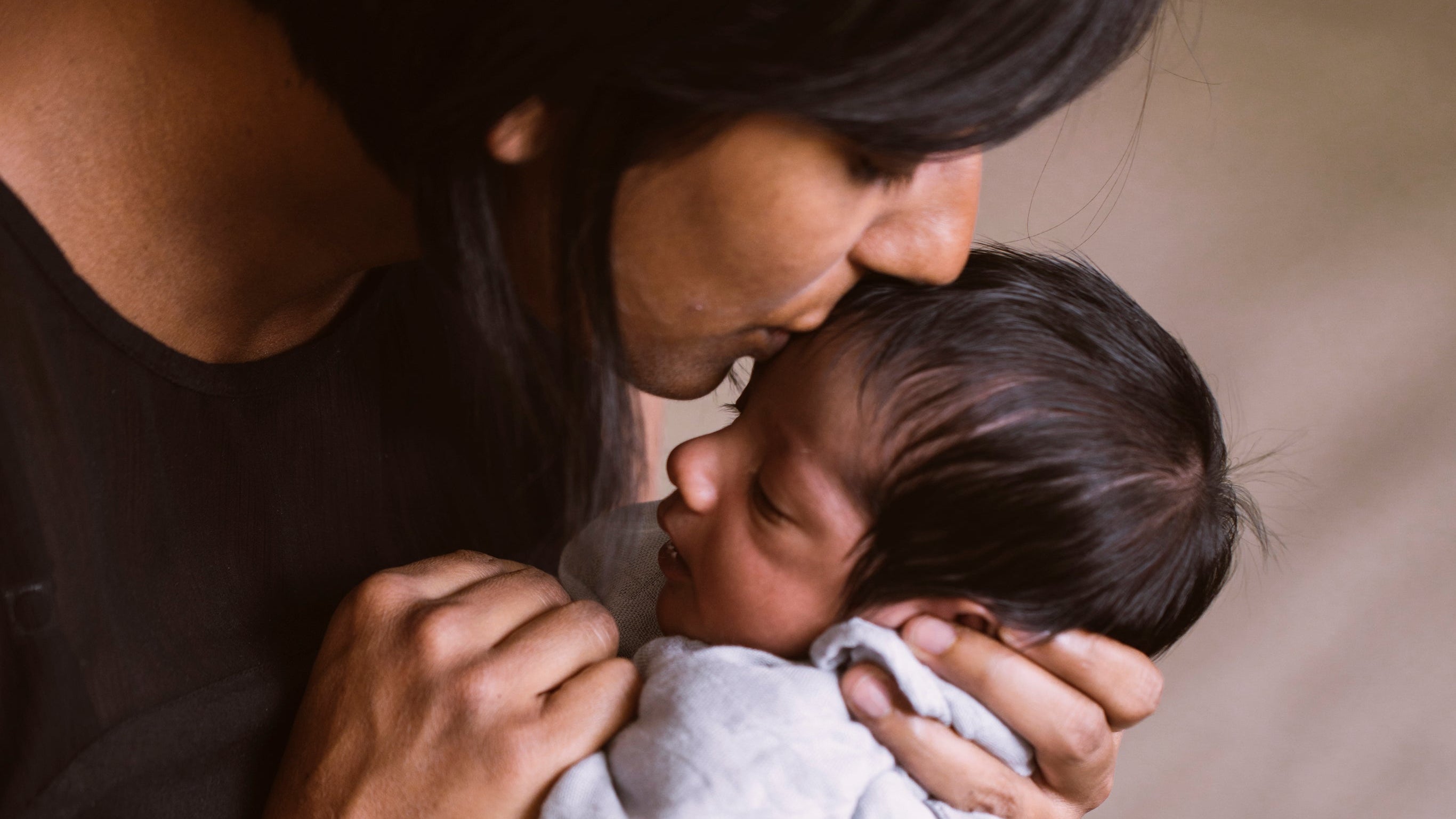 A mother kissing her young infant on the forehead whilst cradling them gently